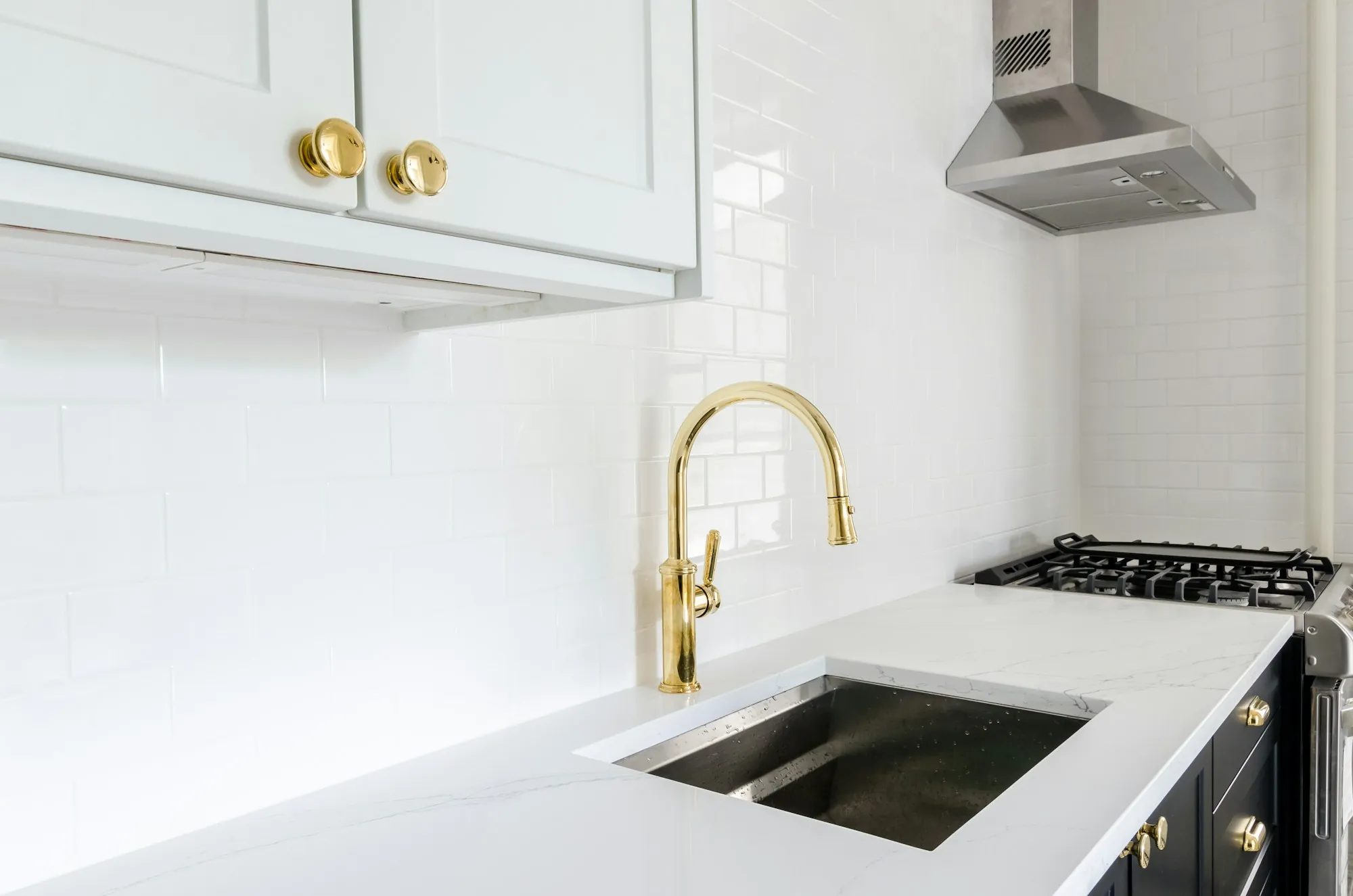 White kitchen with a brass faucet and stainless sink