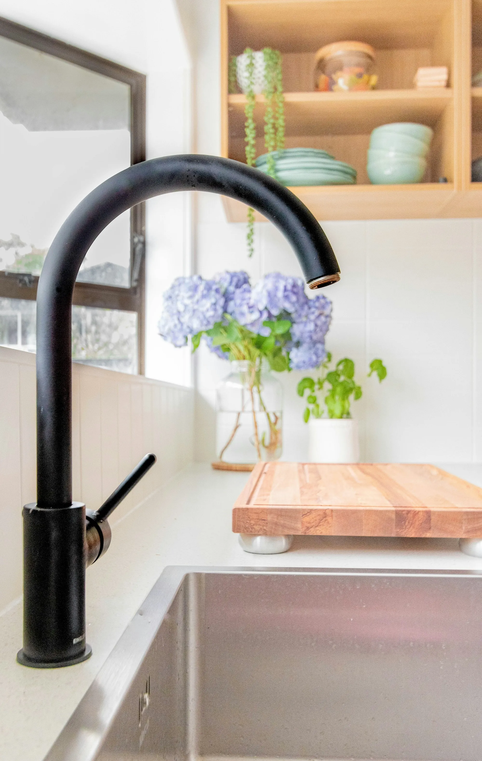 Black kitchen faucet beside a window with fresh flowers