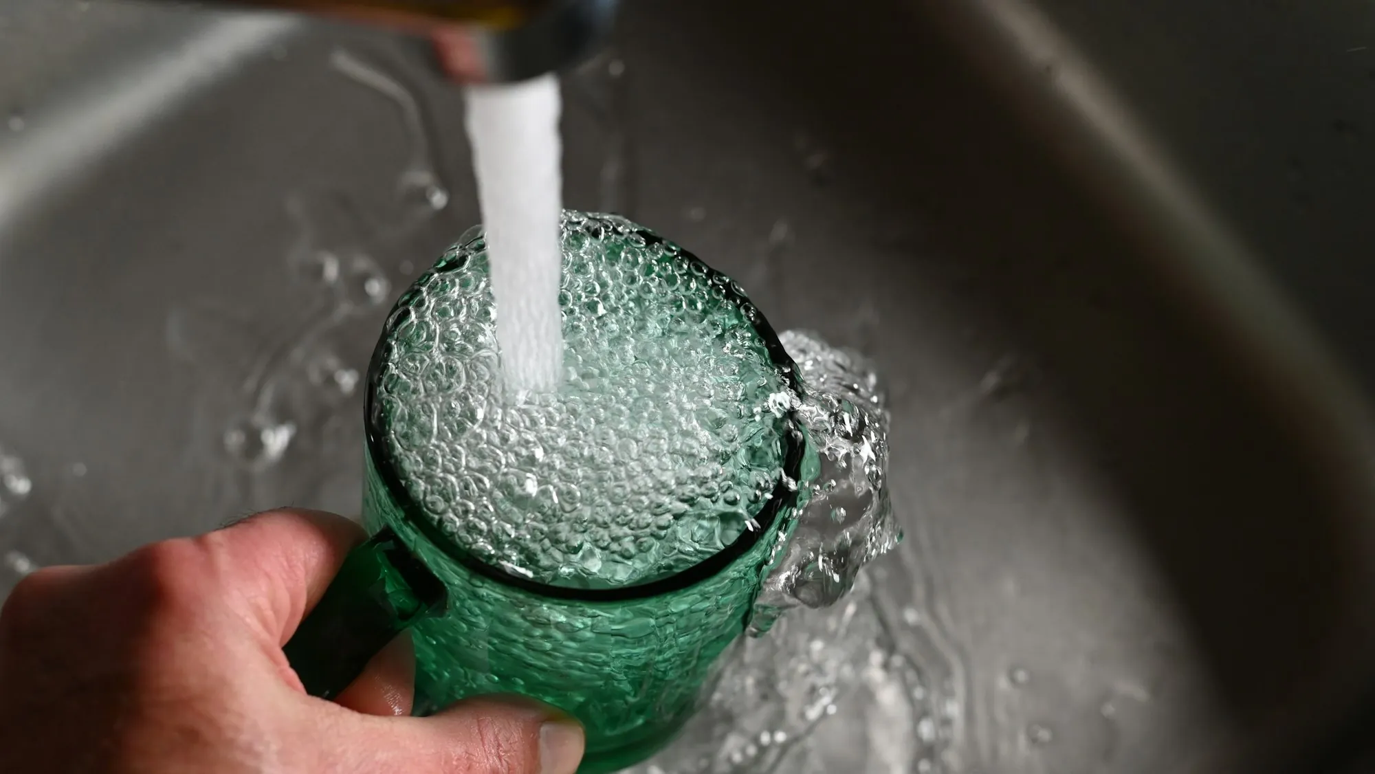 Hand filling a green glass under running tap water